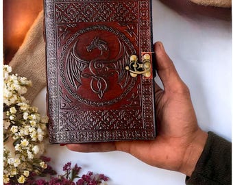 May include: A brown leather journal with a dragon design embossed on the front cover. The journal has a brass clasp closure and a decorative border.