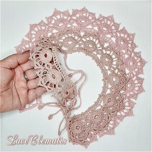 May include: A delicate pink crocheted lace collar with a scalloped edge. The collar is made of multiple layers of lace, creating a beautiful and intricate design. The lace is soft and airy, and it would be perfect for adding a touch of elegance to any outfit.