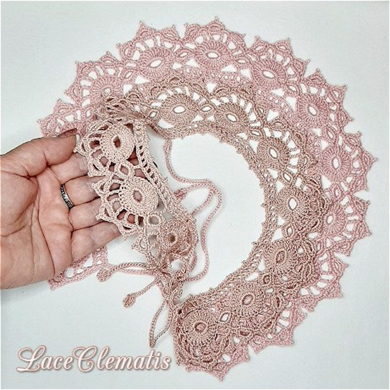 May include: A delicate pink crocheted lace collar with a scalloped edge. The collar is made of multiple layers of lace, creating a beautiful and intricate design. The lace is soft and airy, and it would be perfect for adding a touch of elegance to any outfit.