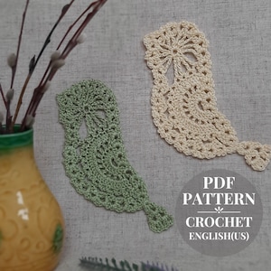 Könnte beinhalten: Zwei Häkelmuster in Form eines Vogels, eines in Grün und eines in Creme. Die Muster befinden sich auf einem beigefarbenen Stoffhintergrund. Der Text "PDF PATTERN CROCHET ENGLISH(US)" befindet sich unter den Mustern.