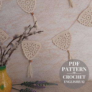 May include: A crochet garland with white triangle flags and tassels. The garland is hanging on a wall with a vase of pussy willow branches in the foreground. The text "PDF PATTERN CROCHET ENGLISH(US)" is visible in the lower right corner of the image.