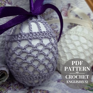 May include: Two crocheted Easter egg covers, one in purple and one in white, with a purple ribbon tied around the purple egg. The text "PDF PATTERN CROCHET ENGLISH(US)" is on a gray circle.