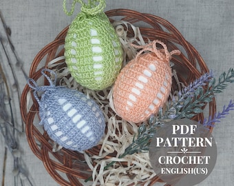 Può includere: Tre uova di Pasqua all'uncinetto in un cesto. Le uova sono verdi, arancioni e blu con strisce bianche. Il cesto è fatto di vimini marrone intrecciato. L'immagine include il testo "PDF PATTERN CROCHET ENGLISH(US)".