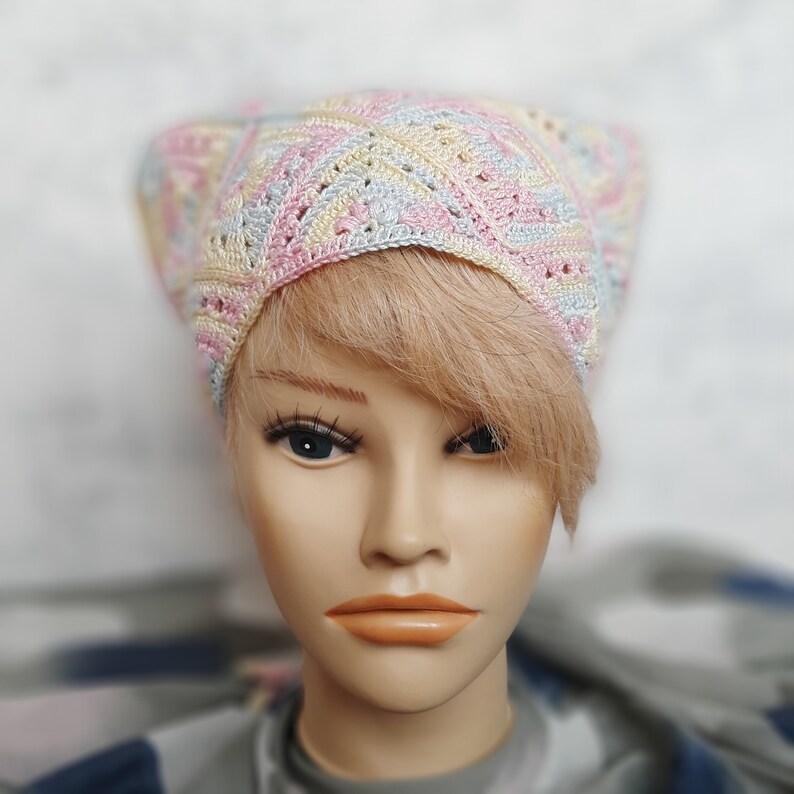 May include: A crocheted hat in pastel pink, blue, and yellow colors. The hat has a geometric pattern and is made with a soft yarn.