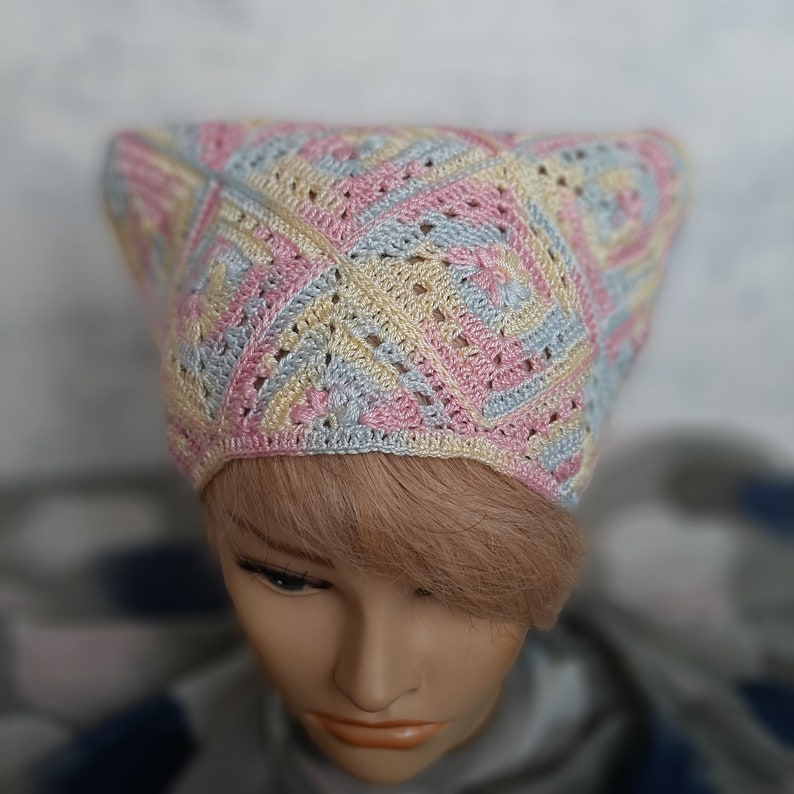 May include: A crocheted hat in pastel pink, blue, and yellow colors. The hat is made with a square stitch pattern and has a pointed crown.