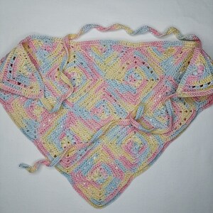 May include: A crocheted triangular shawl in pastel pink, blue, and yellow with a square pattern. The shawl has a long tie that can be used to wrap around the neck.