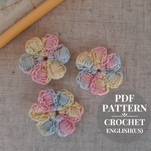 Op de afbeelding: Drie gehaakte bloemen in roze, geel en blauw. De bloemen zijn gemaakt met een granny-steekpatroon. De afbeelding bevat de tekst "PDF PATTERN CROCHET ENGLISH(US)".