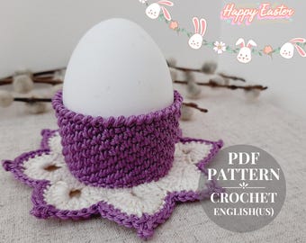 May include: Purple crocheted egg cozy with a white crocheted flower base. The cozy is designed to hold an egg. The image includes the text "PDF PATTERN CROCHET ENGLISH(US)".