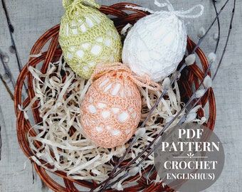 Può includere: Tre copriuova pasquali all'uncinetto nei colori pastello: verde chiaro, bianco e pesca. Le uova sono adagiate in un cestino di vimini con carta di riempimento e rametti. Il testo "PDF PATTERN CROCHET ENGLISH(US)" è visibile.
