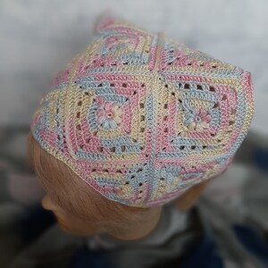 May include: A crocheted headband in pink, blue, and yellow with a square pattern and floral accents.