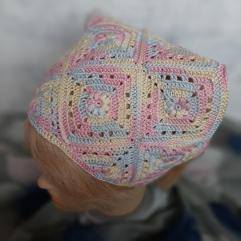 May include: A crocheted headband in pink, blue, and yellow with a square pattern and floral accents.