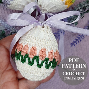 May include: Crochet pattern for an Easter egg ornament. The egg is white with a green and pink trim. The pattern is available in PDF format and is written in English (US).
