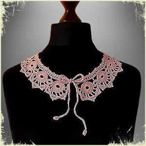 May include: A delicate pink crocheted collar with a tie closure. The collar is made of fine yarn and features a delicate floral pattern.