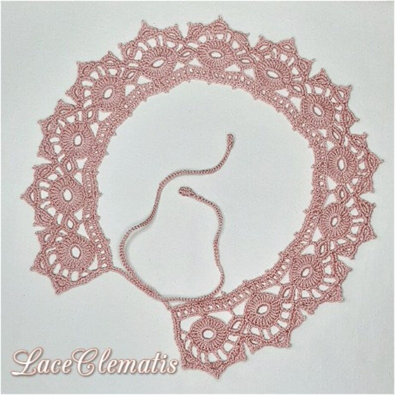 May include: A delicate pink crocheted lace collar with a delicate floral pattern. The collar is tied with a thin pink ribbon.