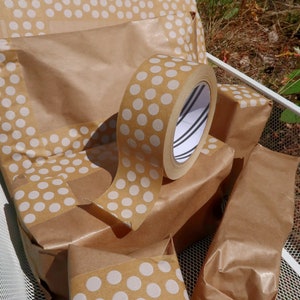 May include: A roll of brown packing tape with white polka dots. The tape is on top of several brown paper packages, also decorated with white polka dots.