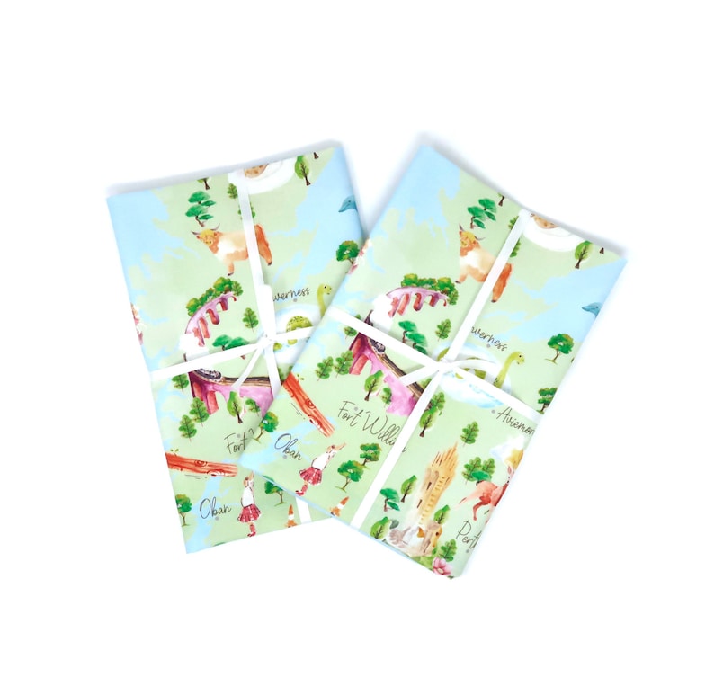 May include: Two blue and green fabric tea towels with a map of Scotland design. The map features various cities and towns, including Oban, Fort William, Inverness, and Aberdeen. The design also includes illustrations of Highland cows, Nessie the Loch Ness Monster, and other Scottish icons.
