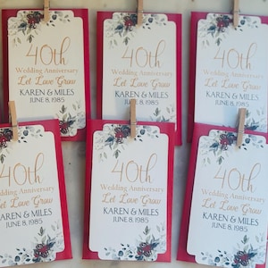 May include: Six red seed packets with a floral design and gold lettering. The packets say "40th Wedding Anniversary Let Love Grow Karen & Miles June 8, 1985".