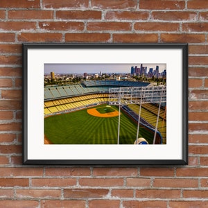 May include: An aerial view of a baseball stadium with a green field and yellow seats. The stadium is surrounded by a city skyline in the distance.