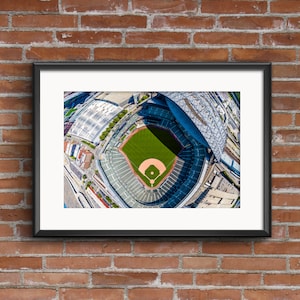 May include: An aerial view of a baseball field with green grass and a dirt infield. The field is surrounded by a large, modern stadium with a retractable roof. The stadium is located in a city with buildings and streets visible in the background.
