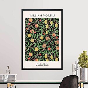 Könnte beinhalten: Ein gerahmter Kunstdruck mit dem Titel William Morris Fruit pattern, der eine botanische Illustration von gelben und orangen Früchten mit grünen Blättern auf schwarzem Grund zeigt, platziert über einem Glastisch mit schwarzem Stuhl und Pflanze.