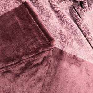 May include: A plush, mauve-colored blanket featuring a soft, velvety texture on one side and a looped, terry-cloth-like fabric on the other. The material is folded to reveal the contrast between the smooth, dense pile and the textured weave.