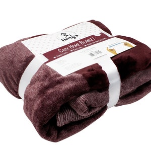 May include: A folded burgundy plush blanket wrapped in a white paper band labeled Henry's Cozy Home Blanket. The packaging features a graphic of hands measuring a 240 cm by 220 cm area, along with text stating Super Fluffy, Easy-Care, and Keeps You Warm and Comfy.