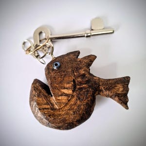 May include: A wooden fish keyring with a blue eye, attached to a silver key and a gold key ring.