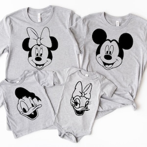 May include: A set of four gray t-shirts featuring black and white cartoon character faces. The shirts feature Mickey Mouse, Minnie Mouse, Donald Duck, and Daisy Duck.