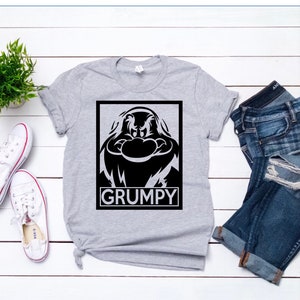 May include: A gray t-shirt with a black and white graphic of Grumpy from Snow White and the Seven Dwarfs. The graphic is in a black square with the word "GRUMPY" printed in white below it.