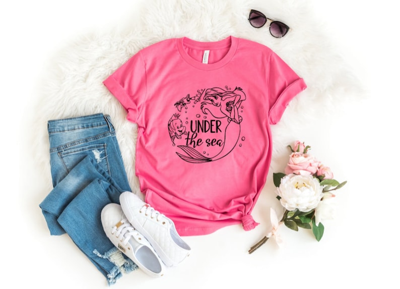 Pode incluir: Camiseta rosa com um gr&aacute;fico preto e branco de Ariel e Linguado da Pequena Sereia. O gr&aacute;fico inclui o texto "Under the Sea".