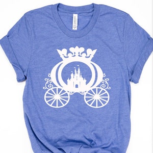 May include: A blue t-shirt featuring a white design of a carriage with a castle inside. The carriage has a crown on top and ornate details.