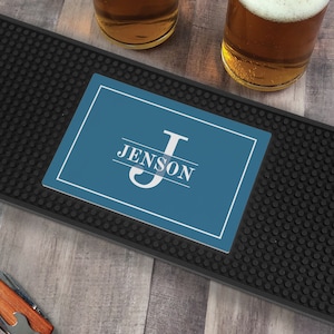 May include: A black bar mat with a blue personalized coaster featuring the initial "J" and the name "Jenson".