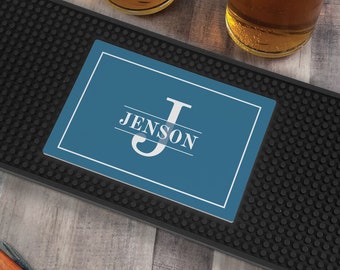 May include: A rectangular black rubber bar mat with a textured surface featuring a blue center panel. The panel displays a white border, a large letter J, and the text JENSON centered horizontally across the letter in a white serif font.