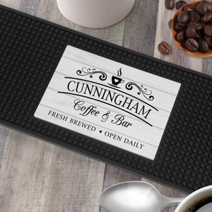May include: Black bar mat with a white rectangular insert featuring the text "Cunningham Coffee & Bar Fresh Brewed - Open Daily" with a stylized coffee cup graphic.
