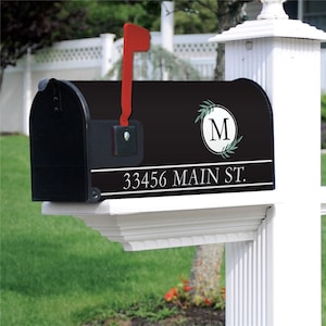 May include: Black mailbox with a red flag, featuring the address "33456 MAIN ST." in white text. The mailbox has a decorative circular design with the letter "M" and olive branch accents.