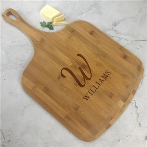 May include: A personalized bamboo pizza serving board with a cursive "W" and the name "WILLIAMS" engraved on the surface.