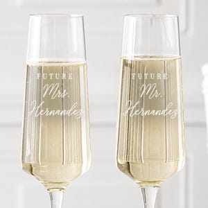 May include: Two clear glass champagne flutes filled with a sparkling liquid. The left glass features white etched text reading Future Mrs. Hernandez, while the right glass features white etched text reading Future Mr. Hernandez in a script font.