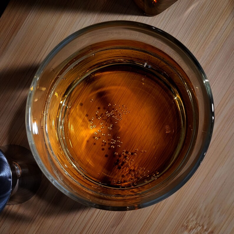 Puede incluir: Primer plano de un vaso lleno de un l&iacute;quido marr&oacute;n dorado, que muestra peque&ntilde;as burbujas subiendo a la superficie.