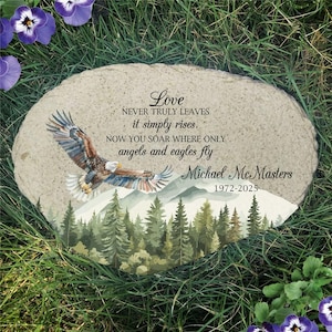 May include: A memorial stone featuring a bald eagle in flight over a forest and mountain landscape. The text reads: Love NEVER TRULY LEAVES it simply rises. NOW YOU SOAR WHERE ONLY angels and eagles fly. Michael McMasters 1972-2025.