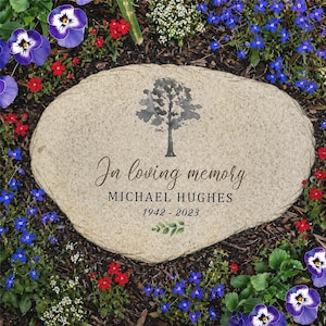 Peut inclure: Une pierre tombale de couleur claire avec le texte "In loving memory" et le nom "MICHAEL HUGHES" ainsi que les années "1942-2023". Un dessin d'arbre à l'aquarelle est au-dessus du texte. La pierre est entourée de fleurs colorées.