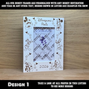 Op de afbeelding: Witte fotolijst met Disney-figuren en de tekst "Disneyland Paris" en "2026". De lijst is versierd met Mickey Mouse, Donald Duck en andere Disney-personages. De foto-opening is 152 x 102 mm.