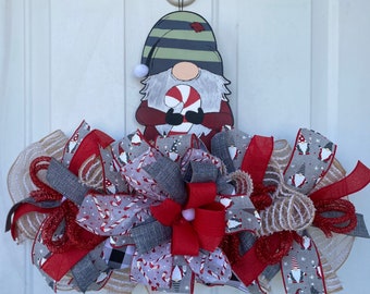 May include: A Christmas gnome wreath with a wooden gnome figure holding a candy cane. The wreath features red, gray, and white ribbons with gnome and candy cane patterns. The wreath is approximately 20 inches wide.
