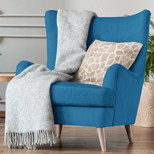 Pu&ograve; includere: Una poltrona blu con una coperta di lana grigio chiaro e un cuscino beige con un motivo geometrico. La poltrona ha gambe in legno e uno schienale imbottito.