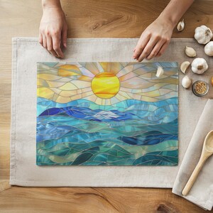 Hands getting ready to use the stained glass style cutting board with a blue and green ocean scene and a yellow sun in the sky.