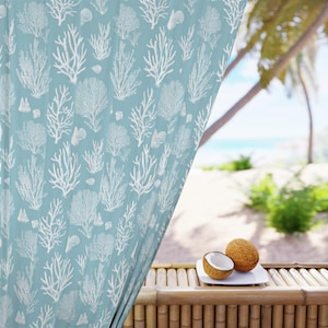 Puede incluir: Cortina azul claro con un estampado de coral y conchas blancas. La cortina está parcialmente corrida, revelando una escena de playa tropical con palmeras y el océano. Dos cocos, uno cortado por la mitad, descansan sobre un plato blanco.