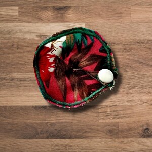 May include: A reusable cloth menstrual pad with a floral print in shades of red, green, and white. The pad has a green trim and a white snap closure.