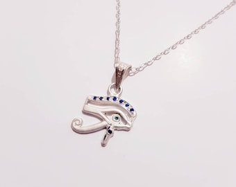 May include: Silver necklace with a blue and green eye of Horus pendant. The pendant is decorated with small blue gemstones.