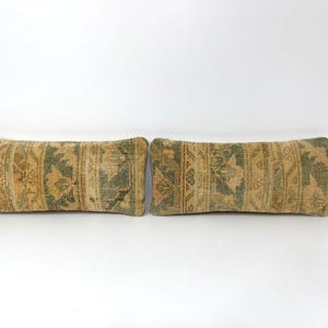 May include: Two rectangular throw pillows with a vintage, patterned design. The pillows feature a mix of tan, green, and peach colors. The design includes floral and geometric elements, creating a rustic aesthetic.