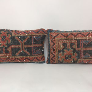May include: Two decorative throw pillows with a traditional rug pattern in shades of red, blue, green, and beige. The pillows are made of woven fabric and have a rectangular shape.