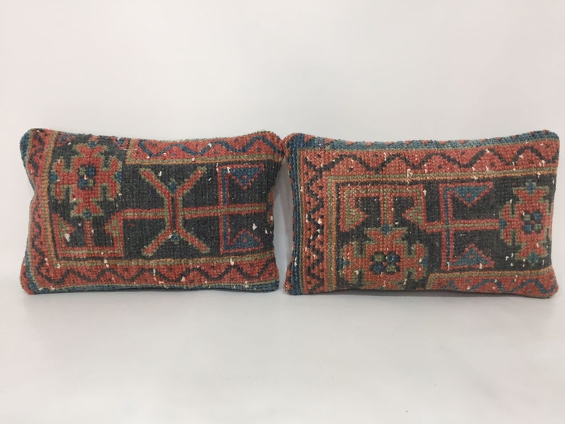 May include: Two decorative throw pillows with a traditional rug pattern in shades of red, blue, green, and beige. The pillows are made of woven fabric and have a rectangular shape.